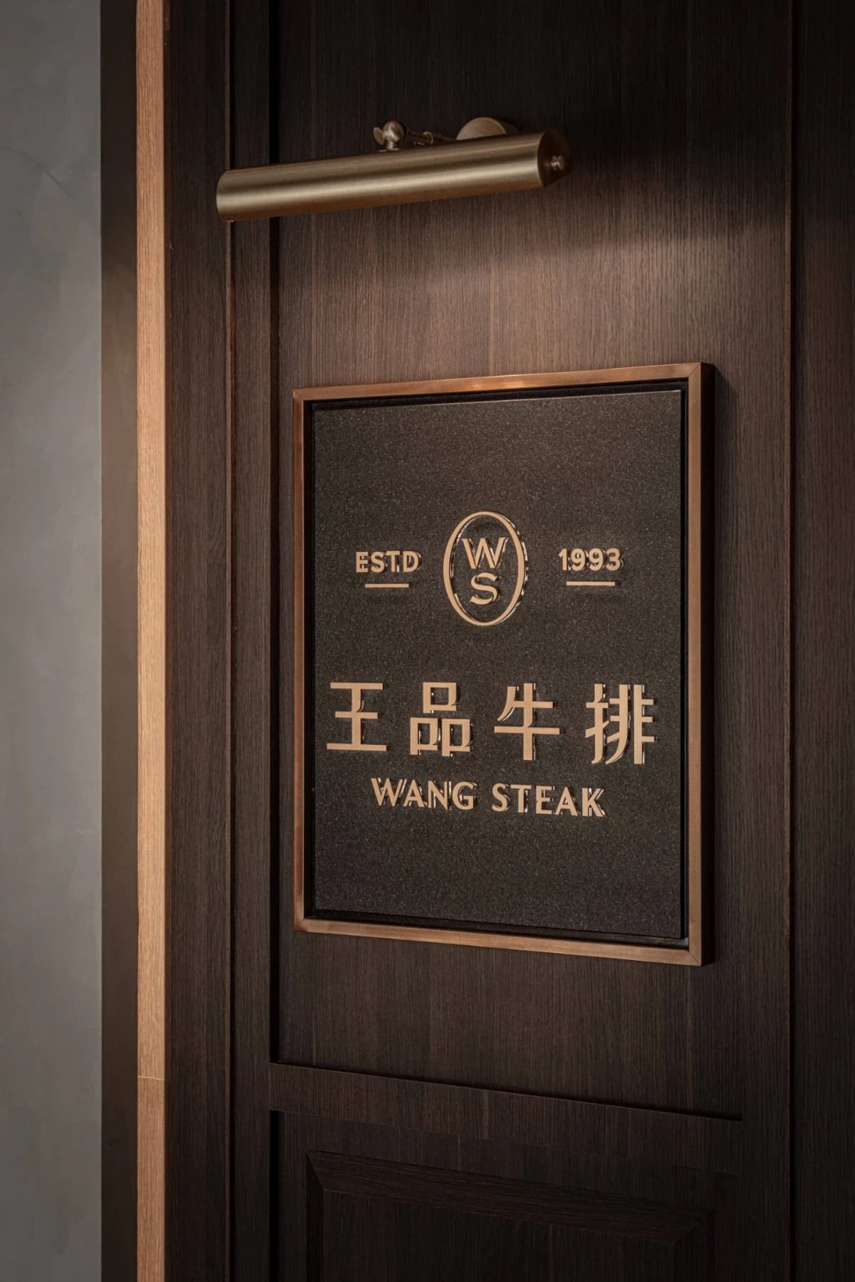 王品牛排裕誠店品牌銘牌結合深色木質與古銅金屬細節，展現精緻餐飲空間質感